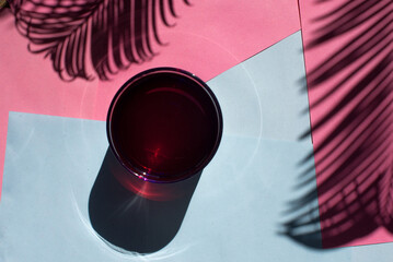 Pink drink in the shade of a palm leaf on a pink and blue background. Summer cocktail concept with palm leaf and palm leaf's shade. A glass of fresh juice. Sumer background.