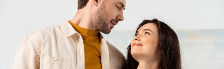 Fototapeta premium Panoramic shot of handsome man looking at smiling girlfriend at home