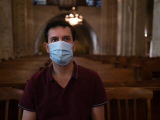Front view of a man wearing a surgical mask praying in a church