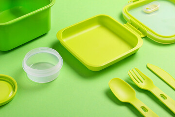 Green plastic lunch box with fork, spoon, knife on green background.Top view,flat lay. Food container for school and office.Copy space.