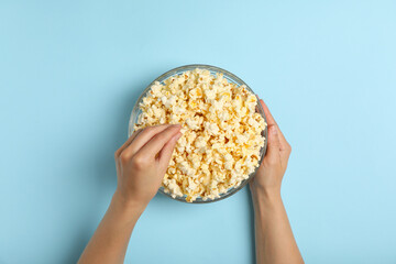 Male hands and bowl with popcorn on blue background