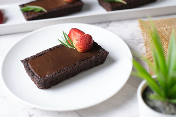 Rectangular chocolate tart with strawberry in white plate set in cafe table.