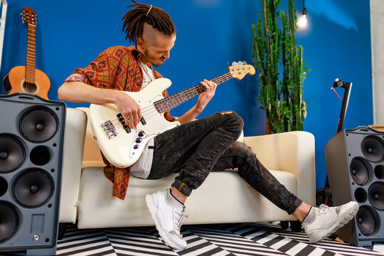 Young caucasian man with dreadlocks playing electric guitar in his room