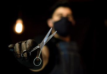 Obraz premium barber holding scissors with one hand on dark background wearing a face mask