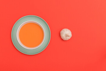Gazpacho bowl on a blue plate and garlic on red background.