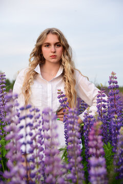 A girl with long blond hair, poses against a background of blooming lupines.