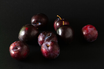 Stack of purple plums on black background.