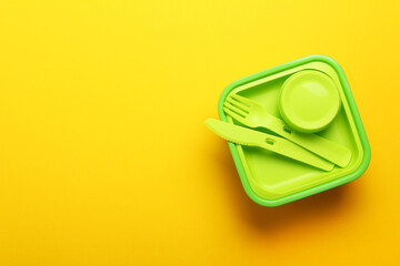 Green plastic lunch box with fork, spoon, knife on yellow background.Top view,flat lay. Food...