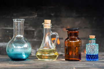Colorful magic potion bottles on wooden table on burning fire in fireplace background. Witch doctor table.