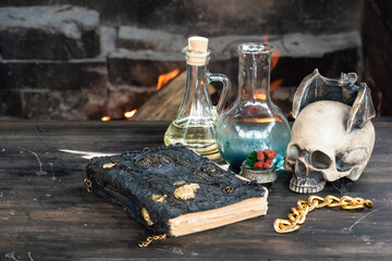 Magic potion and spell book on the table on burning fire in fireplace background. The Witchcraft.