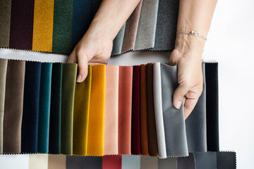 Female hands holding fabric in fabric catalog, woman choosing fabric for new sofa and chairs in new...