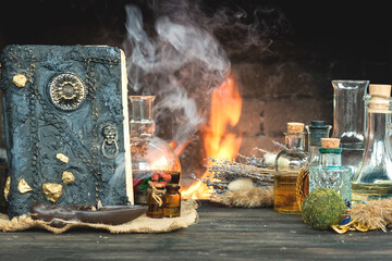 Magic potion and spell book on the table on burning fire in fireplace background. The Witchcraft.