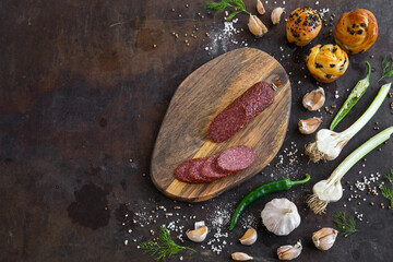 Food background. Kitchen cutting board with sausage on the vintage sharp brown table with spices, homemade bread and vegetables. Top view. Copy space.
