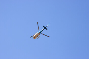 Blue and White helicopter flying in the sky. Helicopter is viewed from below on the ground
