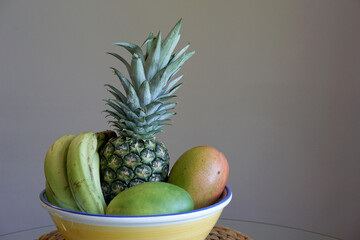 Ceramic blow of  various of fruits, there are pineapple, mangoes, bananas on gray background 