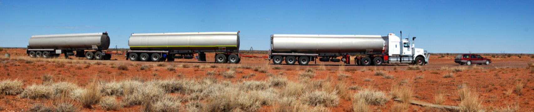 Huge Australia Road train comparison with station wagon car in the red dirt outback