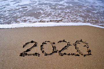 The year 2020 is drawn on sand against the sea
