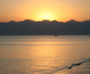 Blurred sunset background - sea and mountains in the golden rays of the sun