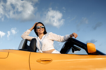 Attractive young woman sitting in yellow convertible car. Freedom, travel and careless concept.