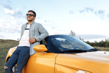Handsome smiling young man staying beside yellow convertible car.
