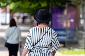 woman in striped clothes and with a black hat on a city street, rear view