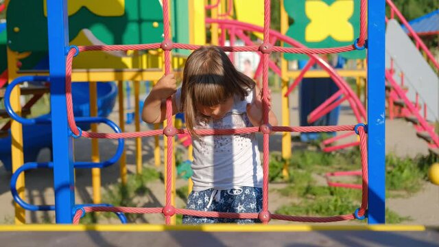 Child girl playing and laughing on the playground, riding on the carousel, climbing the wall.