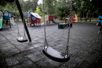 Plastic and wet swings in an empty playground during a rainy summer day.