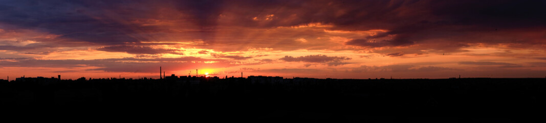 Panoramic view Red bright sunset over the city. City industrial landscape. The rays of the setting sun illuminate the industrial city.