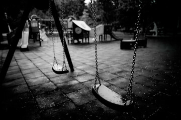 Plastic and wet swings in an empty playground during a rainy summer day.