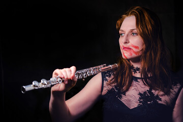 Halloween musician with flute on black background, copy space. Evil woman vampire with lipstick smeared on her face, closeup portrait