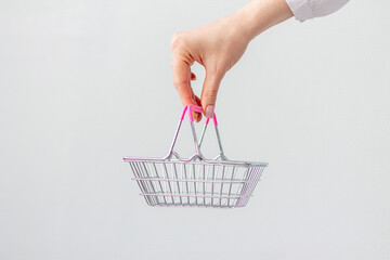 Fototapeta premium Close-up of a woman's hand horizontally holding a toy small metal shopping basket with a pink plastic handle isolated on a white background. copy space for advertising. The concept of shopping.