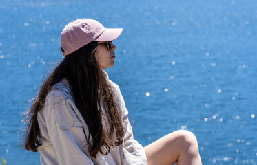 long hair brunette girl in short jeans, cap and sweatshirt enjoying the sun and the views of a mountain lake on vacation.