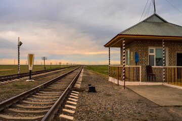 Fototapeta na wymiar Railroad crossing. Railway at sunset. Rails, sleepers, earthen mound. Movement control center at the crossroads. Barrier Control Center. Sky and clouds at sunset.