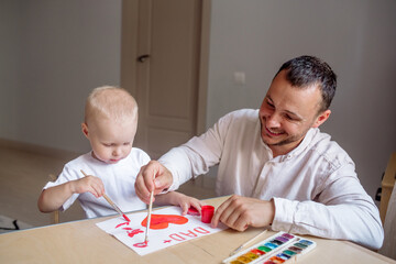 Little boy 2 years old makes a card for the holiday Father's Day with his bearded young father