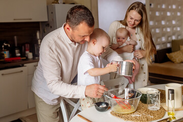 Little boy 2 years old preparing dough with dad, mom and newborn sister in the kitchen at home
