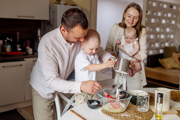 Little boy 2 years old preparing dough with dad, mom and newborn sister in the kitchen at home
