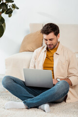 Smiling freelancer using laptop while sitting on floor in living room