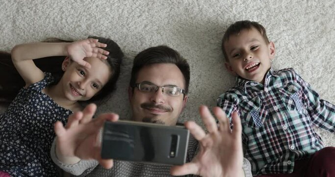 Father and children are lying on the floor and making video call to relatives. Concept of technology, new generation,family, connection, parenthood.