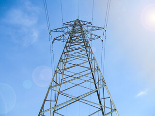 Electric power transmission lines on high voltage towers with blue sky and sun flare.