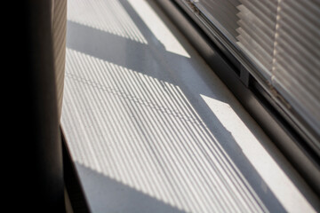 Fototapeta na wymiar Shadow and light through blinds window on window sill. Morning light and shadow. Curtain on the left. 