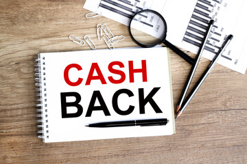 Cash back, message on a white notebook near financial charts, magnifiers on a wooden table