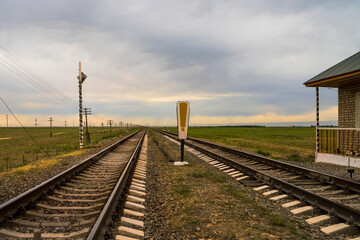 Fototapeta premium Railroad crossing. Railway at sunset. Rails, sleepers, earthen mound. Movement control center at the crossroads. Barrier Control Center. Sky and clouds at sunset.
