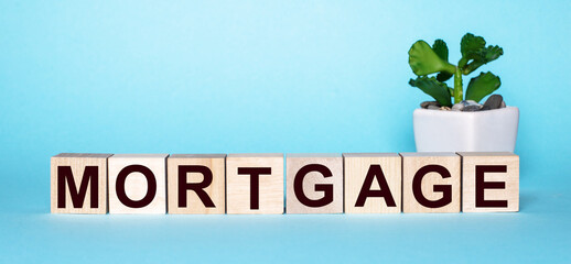 The word MORTGAGE is written on wooden cubes on a blue table near a flower. Business concept