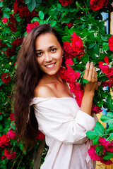 Photo of a beautiful girl in red roses. Portrait of a young woman with flowers. Brunette with flowers.