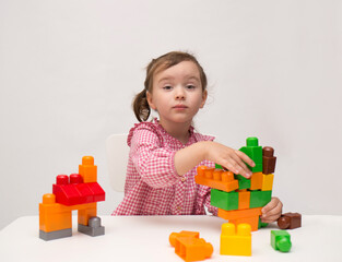 A smart little girl collects a multi-colored construction kit at a table on a white isolated background