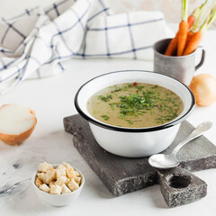 Homemade broth in a white bowl on a wooden Board with vegetables, crackers in the background. concept of healthy eating.