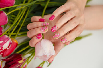 Female hands with tender spring manicure holding pink fresh tulip on flowers background. Nail art, gel nails polish design and beauty concept.