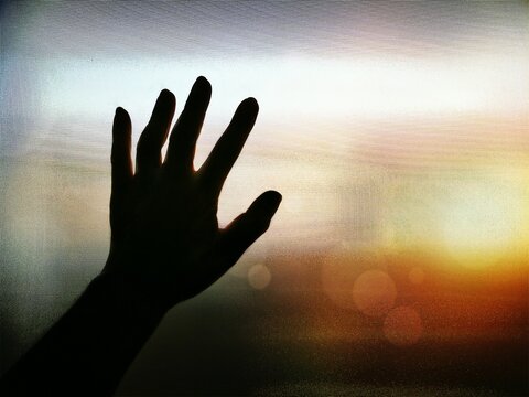 Close-up Of Silhouette Hand Touching Window Curtain