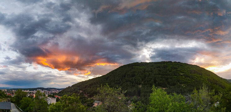 Panoramic view of a lush green hill against a dramatic, cloudy sunset sky in Sliven, Bulgaria