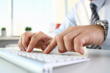 Close up of male company employee working alone while typing on keyboard with window on the background